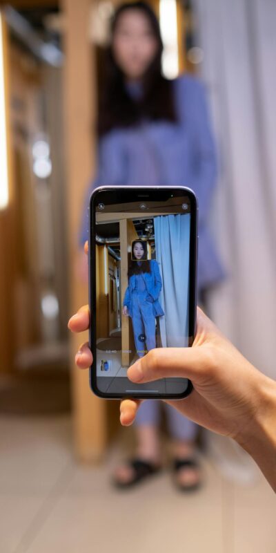 A woman captures an outfit photo with a smartphone in a stylish fitting room.